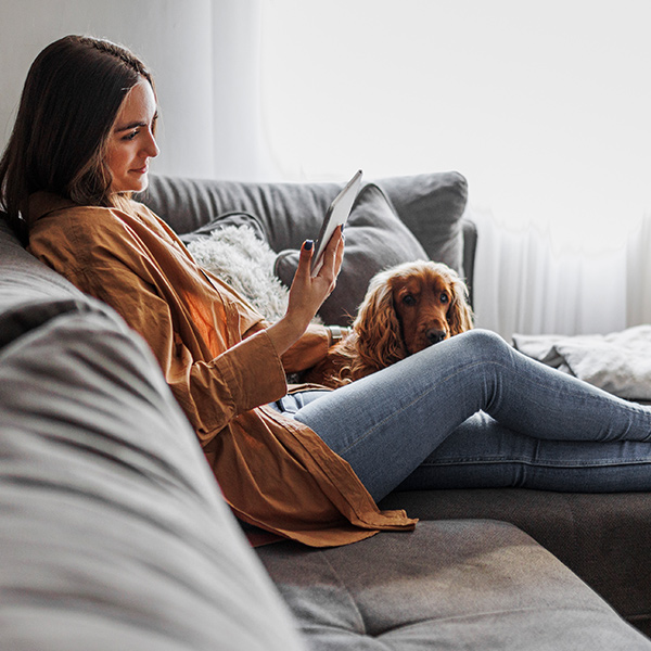 Dame sitter i sofaen med sin hund og leser aktuelle nyheter